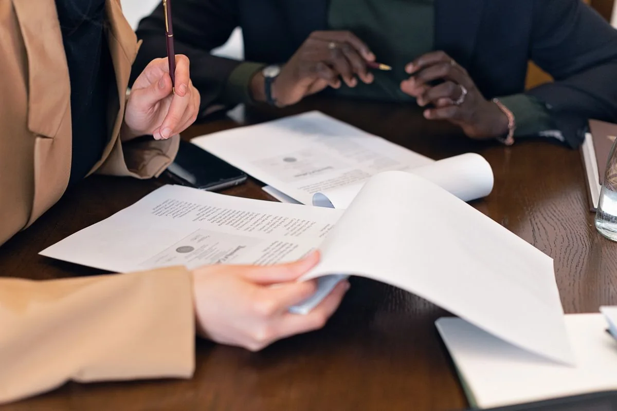 Colleagues examine documents together at a desk.