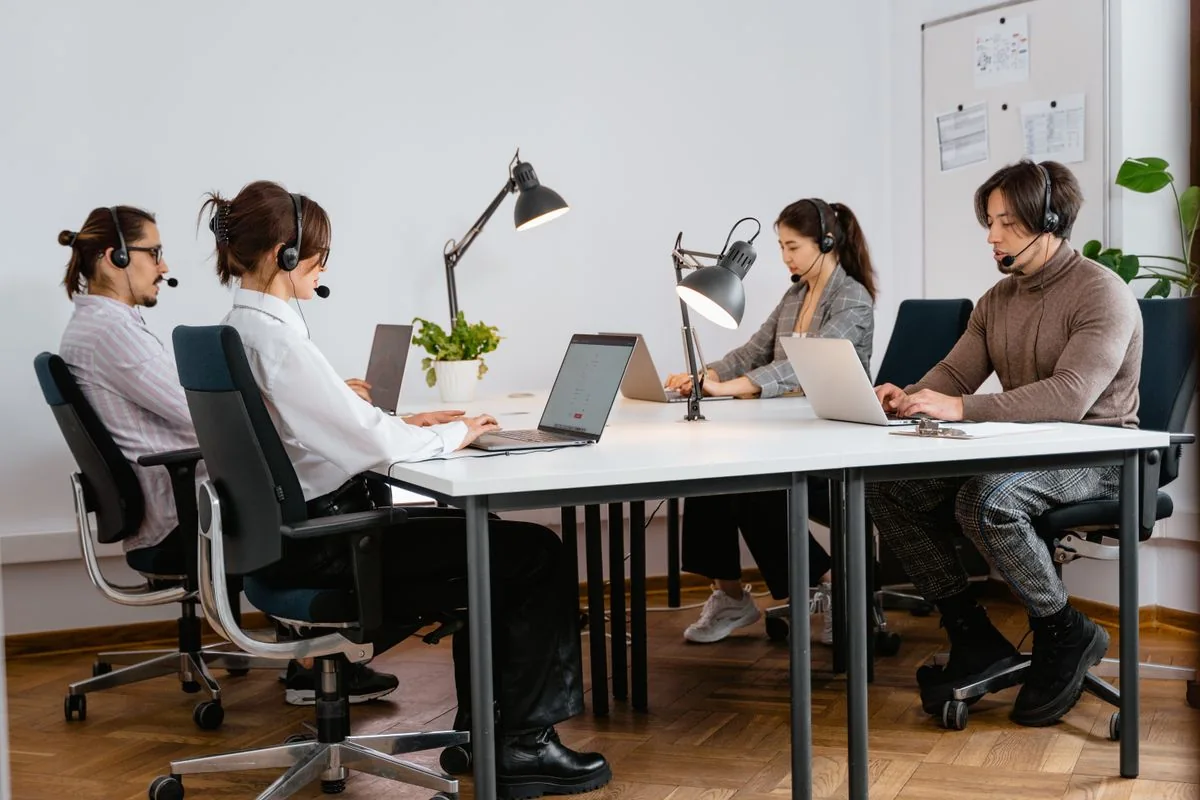 A team wearing headsets works at laptops in a call centre.