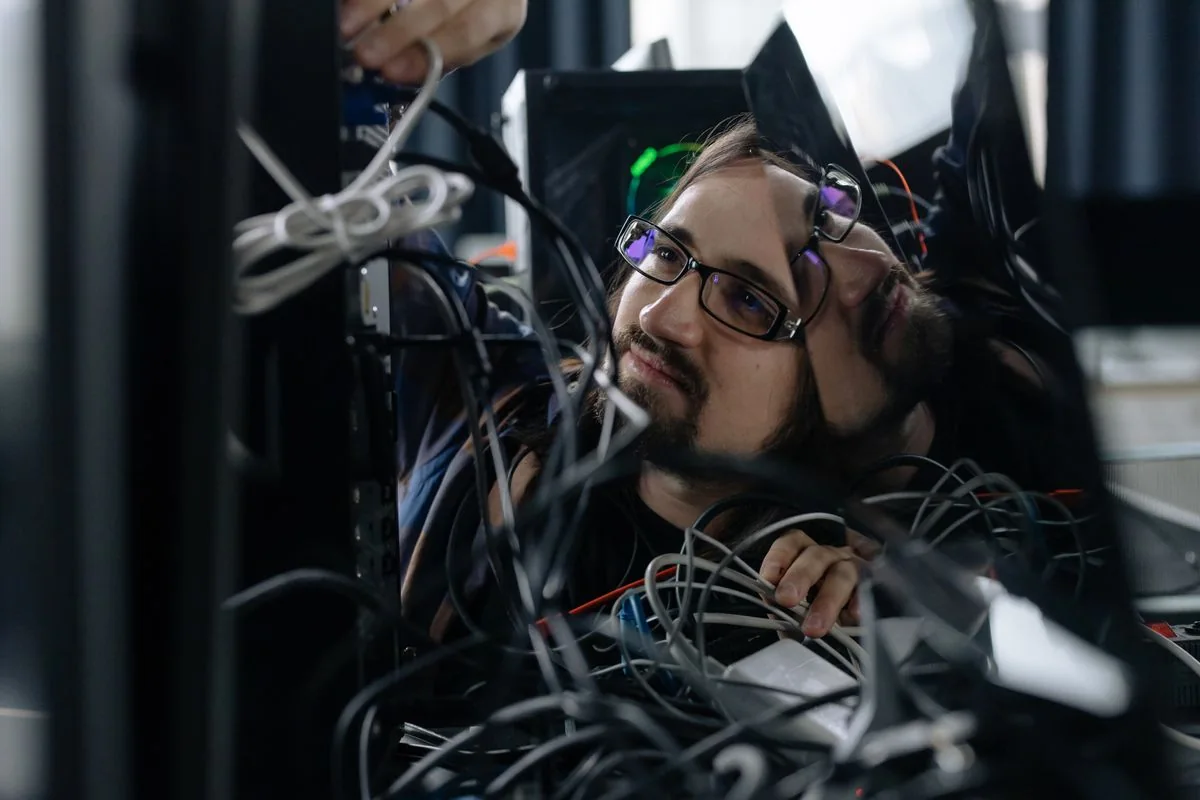 A technician connects cables behind an office workstation.