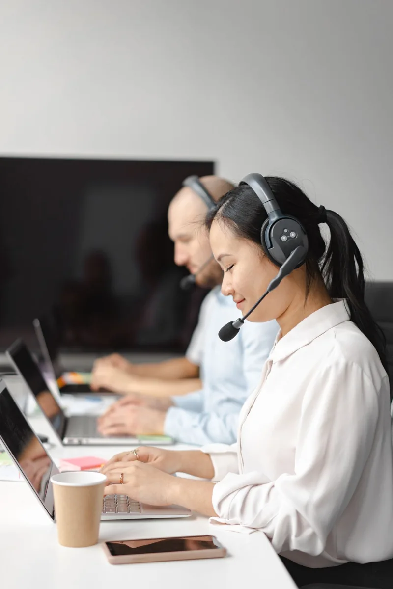 Customer service colleagues wearing headsets work at their desks.