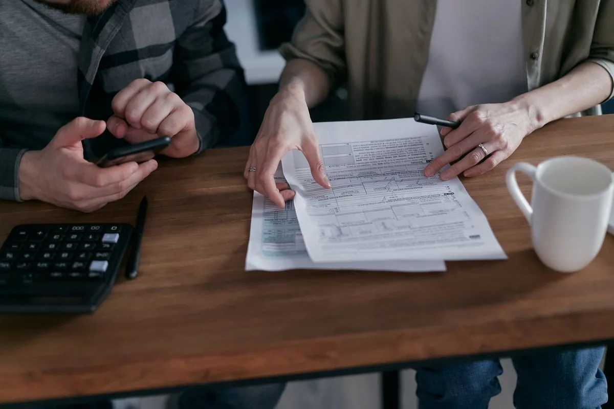 Two people review financial documents with a calculator and phone.