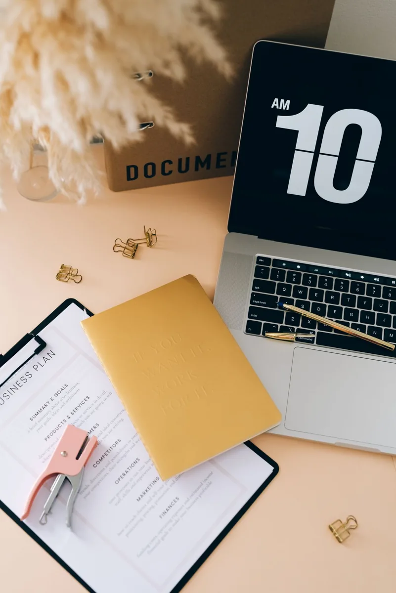 A business plan clipboard and stationery sit beside a laptop.