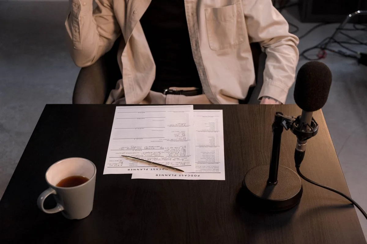 A microphone, paper notes and a coffee cup sit on a recording desk.
